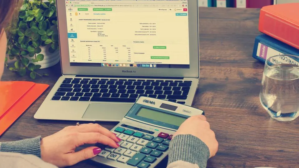 Student using a calculator next to a spreadsheet on a laptop