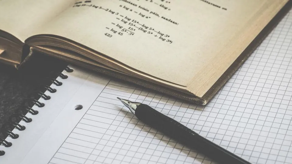 Maths textbook open beside a pen and squared paper